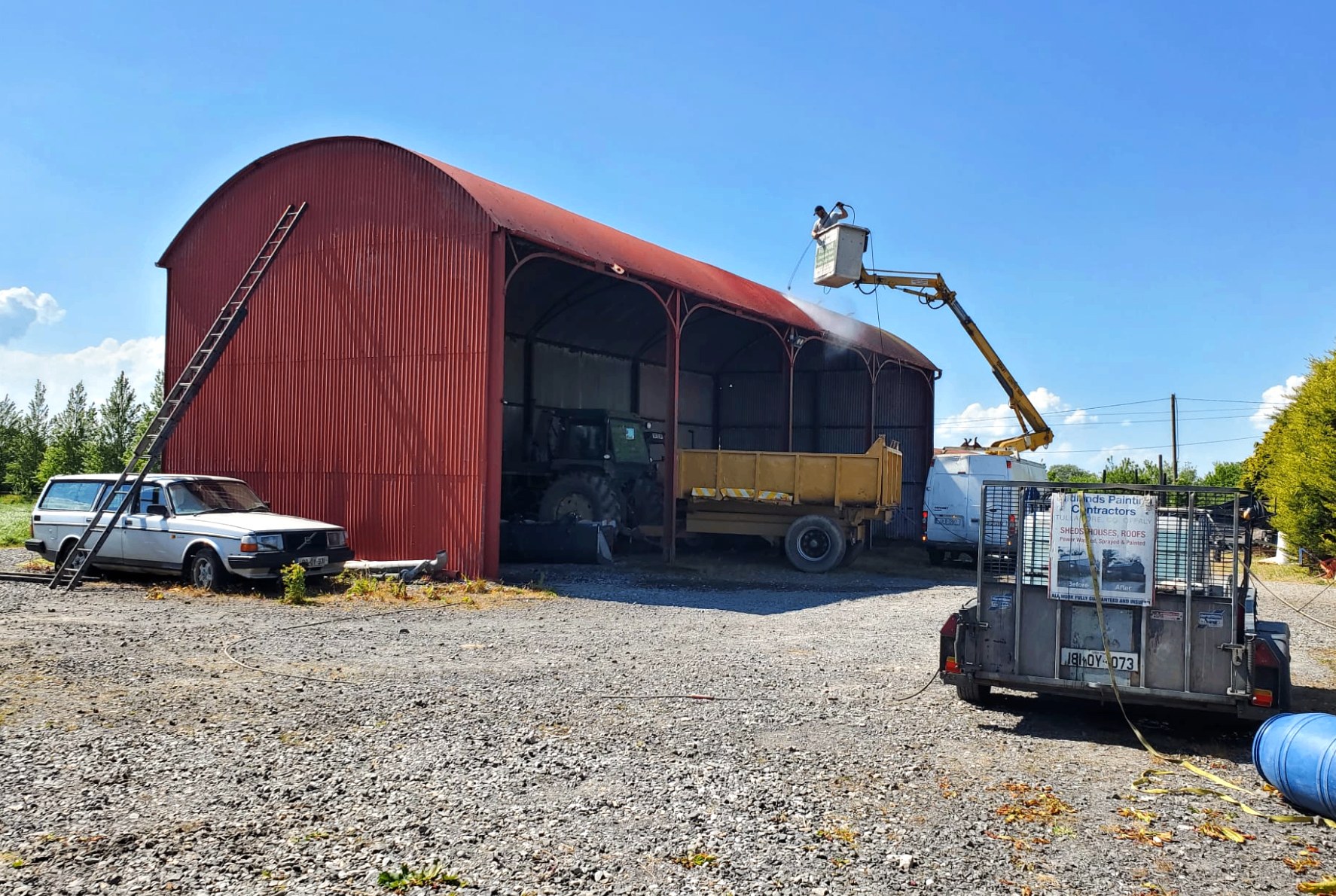 Red barn being sprayed from a cherry picker on a sunny day