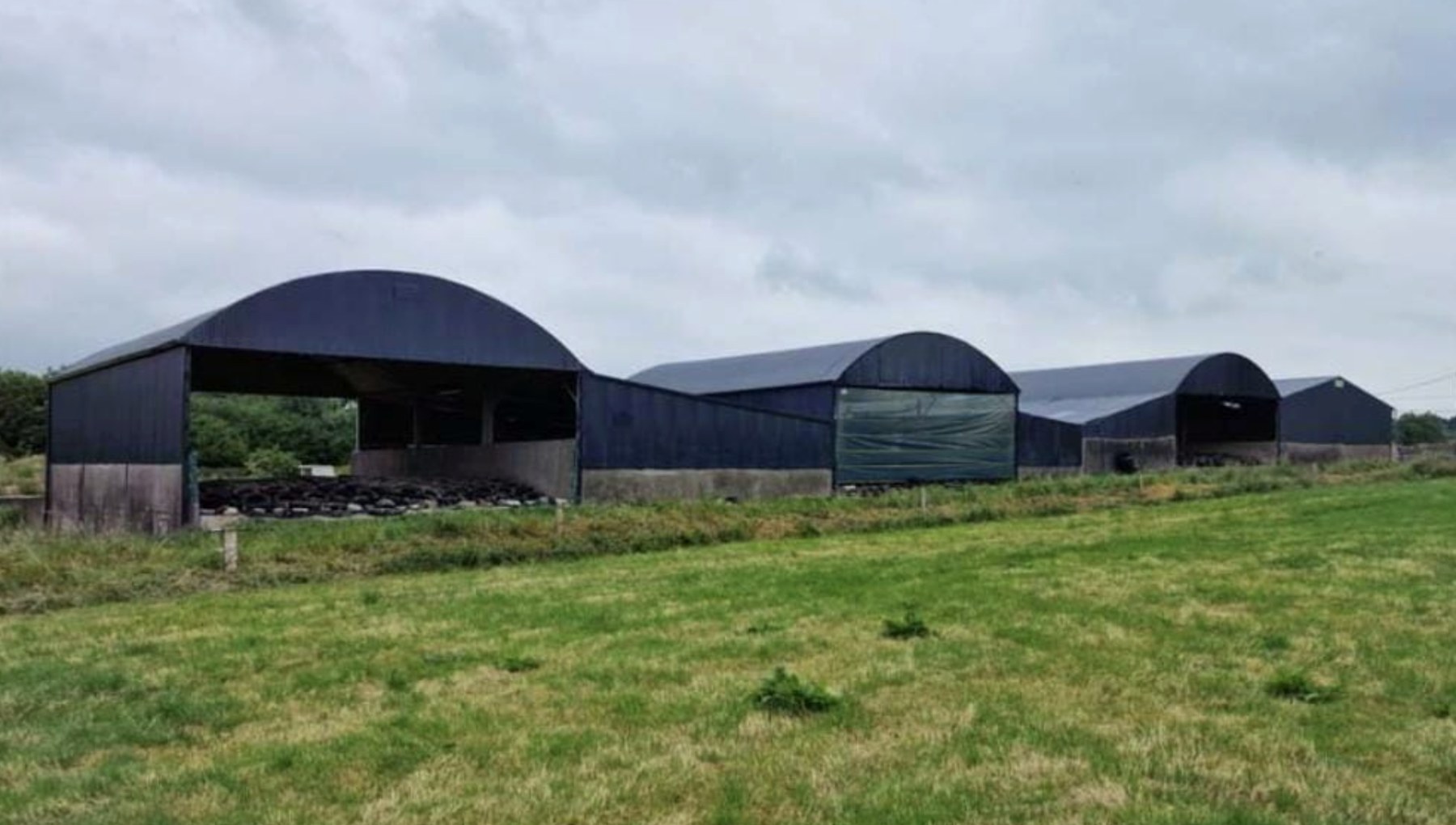 Row of black-painted arched farm sheds on a working yard