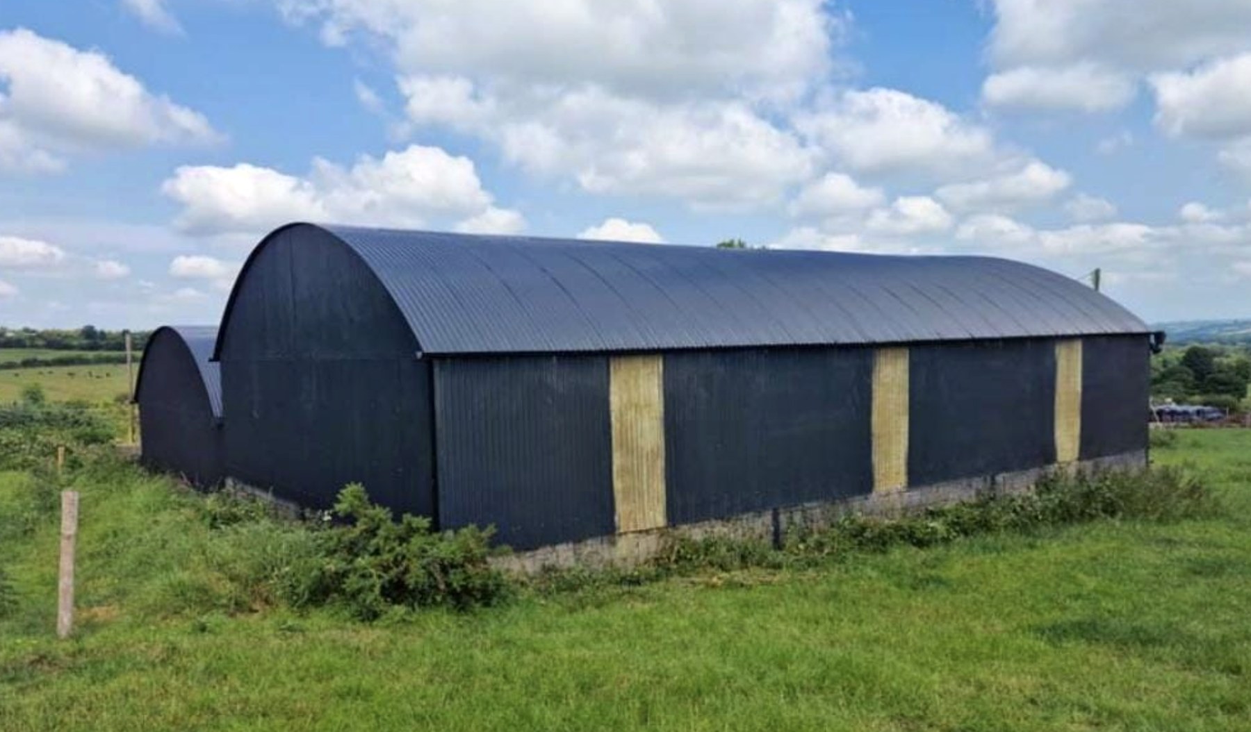 Freshly sprayed black curved-roof farm shed in a green field